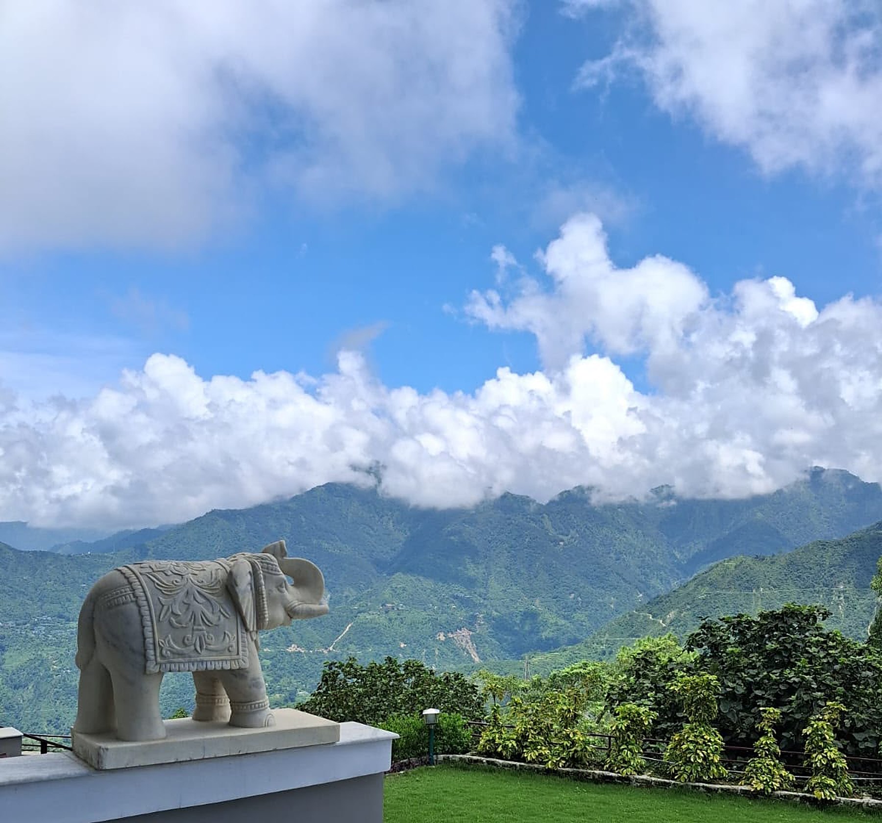 A carved marble elephant watching over green Himalayan ridges and drifting cloud